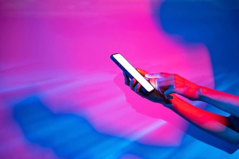 A hand holds a glowing smartphone against a vibrant backdrop of neon lights, showcasing futuristic