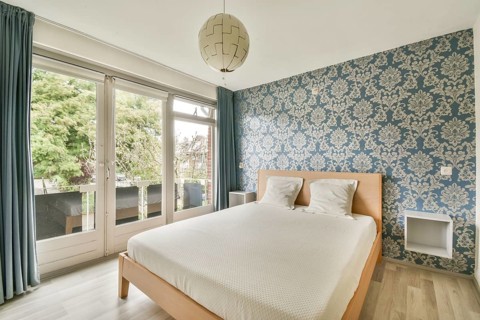 A cozy bedroom features a large bed with white bedding against a stunning blue floral wallpaper.