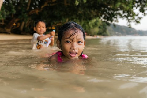 Two children enjoy playing in the ocean water on a beach in the Philippines. A girl in the