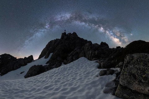 A lone figure stands on a snowy Icelandic peak beneath a stunning Milky Way sky The scene captures