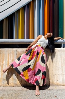 A woman in a vibrant, colorful outfit leans gracefully against a textured wall, showcasing a