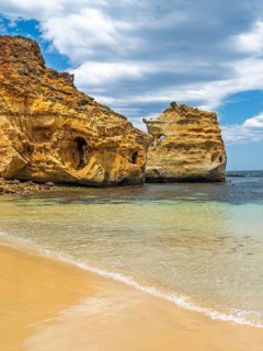 Majestic golden rock formations rise from crystal clear waters, framed by a sandy beach and a