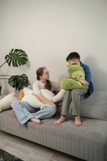 A young sibling duo sits on a sofa, each hugging plush toys. A comforting indoor setting with a