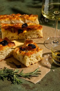 Golden homemade focaccia slices topped with sun dried tomatoes and rosemary, paired with a glass of