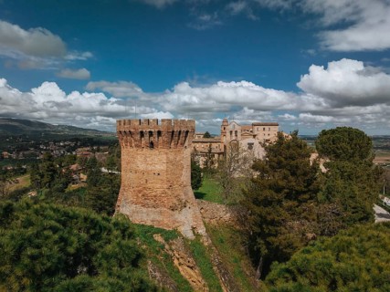 A captivating view of a historic tower and nearby buildings in Treia, Italy. Lush greenery and a