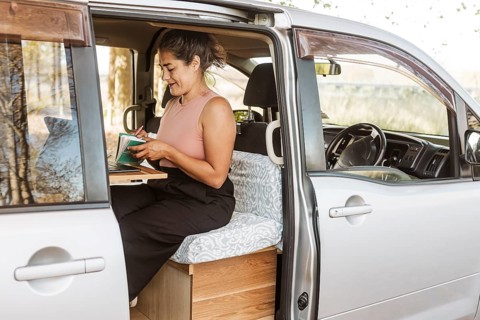 A woman works inside her van, surrounded by the golden hues of autumn in New Zealand. Her mobile