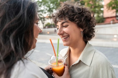 A joyful lesbian couple shares a refreshing drink outdoors, smiling warmly. They enjoy a leisurely