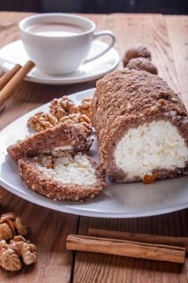 Roll cake with curd and walnuts isolated on white wooden background. close up