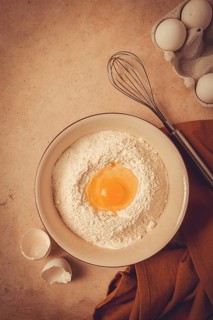 Food background, concept, plate with wheat flour, broken egg, whisk, kitchen towel, on a beige