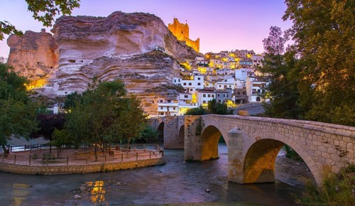 Discover the enchanting evening view of Alcala del Jucar, Spain, where a historic stone bridge