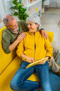 Vertical photo of a relaxed senior couple lying on the sofa using digital tablet