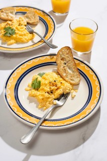 A vibrant breakfast scene featuring creamy scrambled eggs garnished with herbs, served on a