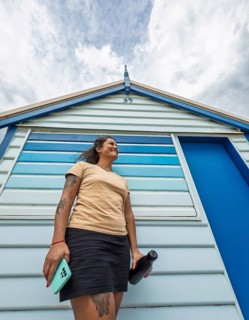 A woman stands in front of the iconic Brighton Bathing Boxes in Melbourne, Australia. The colorful