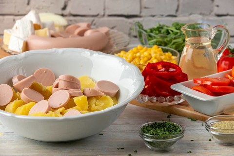 Potatoes and sausage in a bowl surrounded by other ingredients such as peppers, corn, cheese and