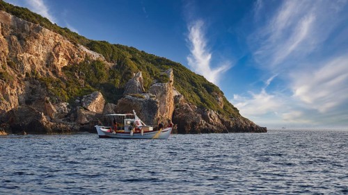 A boat moves along the coast with distinctive cliffs under a sky full of dramatic clouds, morning