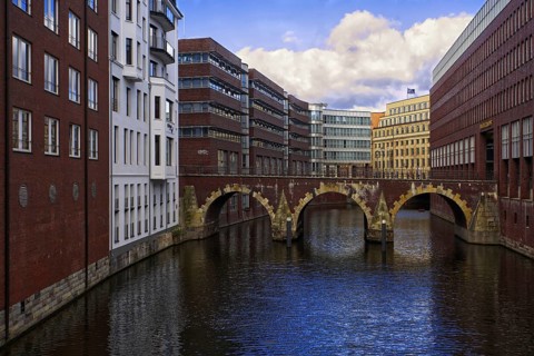 City view with Bleichenfleet canal and old stone bridge surrounded by modern brick buildings, blue