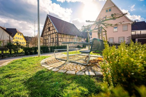 A courtyard with half-timbered houses and a bench in bright sunshine, surrounded by nature,