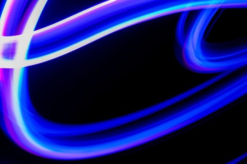 Vibrant blue and purple neon light trails create an abstract design on a dark background, capturing