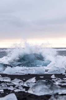 A winter wave crashes onto a black sand beach in Iceland, surrounded by glistening icebergs and a