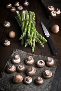 Fresh asparagus bundled with twine and mushrooms artfully arranged on a dark wooden table with