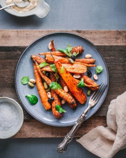 A delicious dish of roasted carrots served on a stylish gray plate, garnished with fresh green