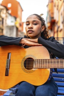 Vertical photo of a confident african american woman leaning on guitar sitting on a bench in the