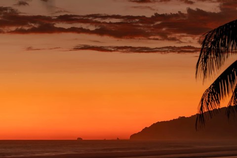 After sunset, the deep red sky glows above palms and ocean spray with views of Corcovado National
