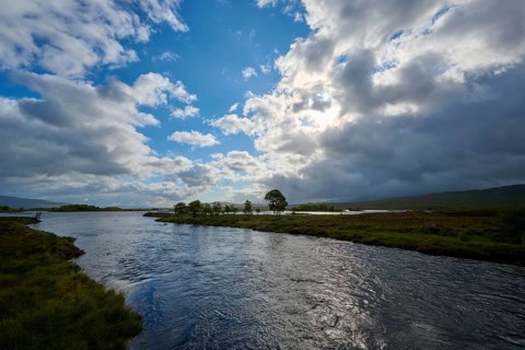 A calm river under a partly cloudy, partly sunny sky in a green landscape, Rannoch Moor, Bridge of