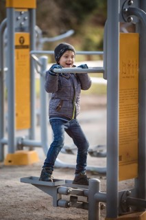 Six years old boy exercises at the outdoor gym. The device has instructions for use in Polish