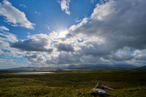 Sunlight breaks through clouds over a vast landscape with mountains in the background, Rannoch