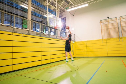 A player jumps up to throw the ball into the basket in a yellow gym, basketball TSV Calw, Germany