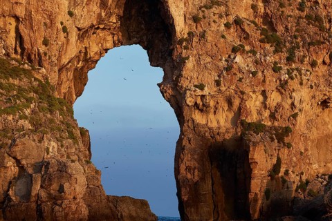A large rock gate with birds in calm evening light over the sea, morning light, Tsichli Babas