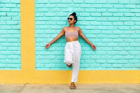 A young latin woman wearing sunglasses, a striped crop top, and white pants poses confidently