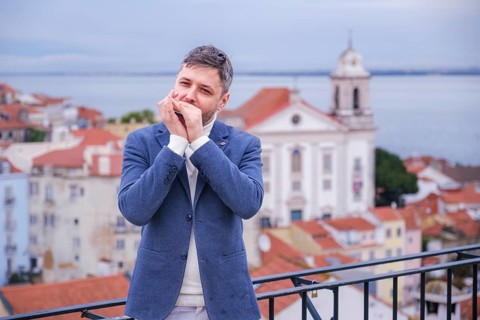 Man musician in a blue blazer and white sweater playing blues on a harmonica with eyes closed,