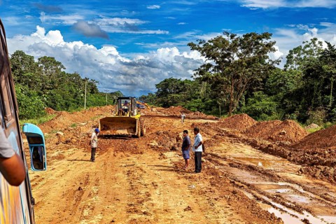 View of a road construction site with people and construction machinery, surrounded by green