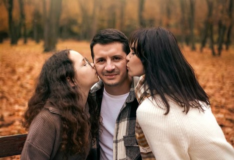A family shares a loving moment in a picturesque forest during autumn. The ground is covered in