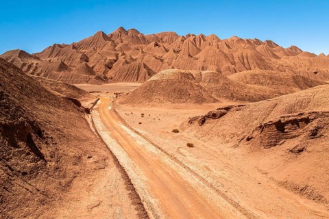Breathtaking view of a rugged desert landscape featuring a winding dirt road, surrounded by hilly