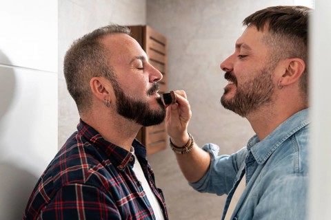 A gay couple enjoys a morning grooming ritual. One partner gently brushes the other's beard,