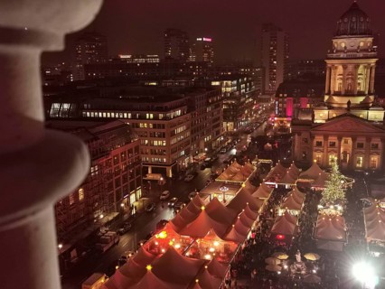 View from above of illuminated Christmas market at Gendarmenmarkt at night, with tents and festive