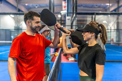 Two adult pickleball players high fiving with their paddles, showing teamwork and sportsmanship