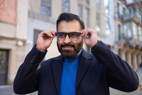 Indian man in a professional outfit adjusts his eyeglasses while standing on a city street. He's