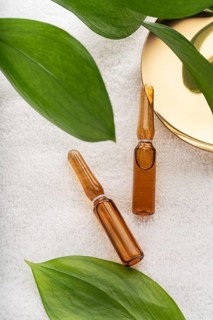 Two glass ampoules filled with anti-aging serum for facial care, resting on a soft white towel,