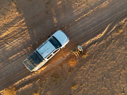 Top Down View, Two travelers sitting next to off-road car on dust road in the desert, aerial view,