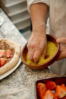 Cropped unrecognizable chef's hand sprinkling toppings on a gourmet pizza with ingredients on a