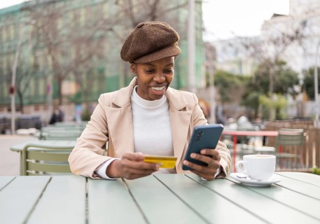 A stylish black woman in an urban setting, enjoying coffee while shopping online with her phone and