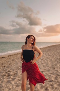 A young woman with red hair stands gracefully on a sandy beach in Miami, dressed in a stylish black