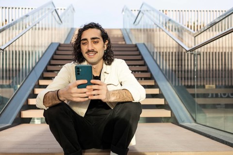 Relaxed man with a mustache sits on outdoor steps, engaging with a smartphone Dressed casually,