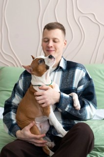 A young man relaxes at home with a playful brown and white dog in his lap, enjoying a moment of