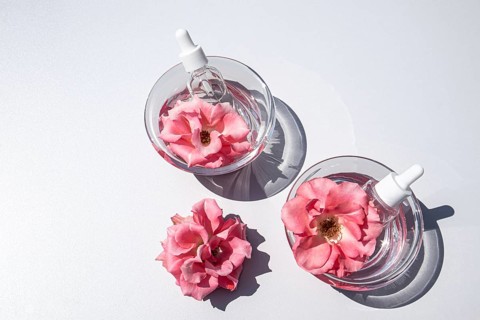 Top view of two glass bowls filled with clear rose water, each containing a pink rose and a dropper
