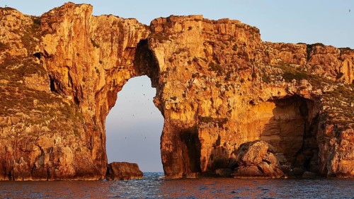 Impressive rock formation with an arch in the sea at sunrise, morning light, Tsichli Babas islet,
